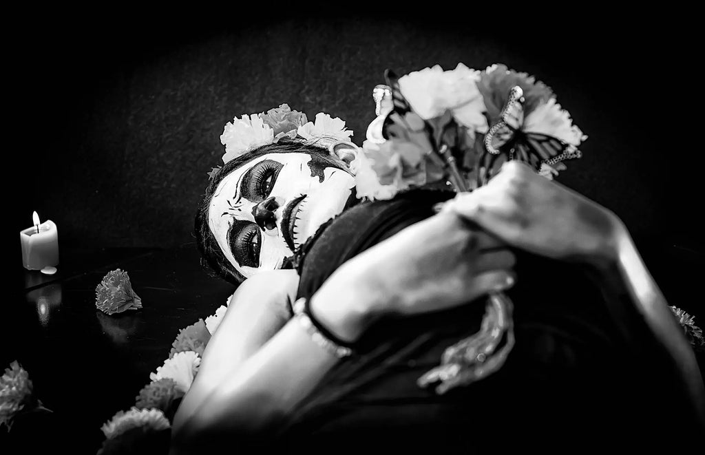 Black and white image of a woman posing for halloween's day of the dead while wearing Mistura Beauty and holding flowers