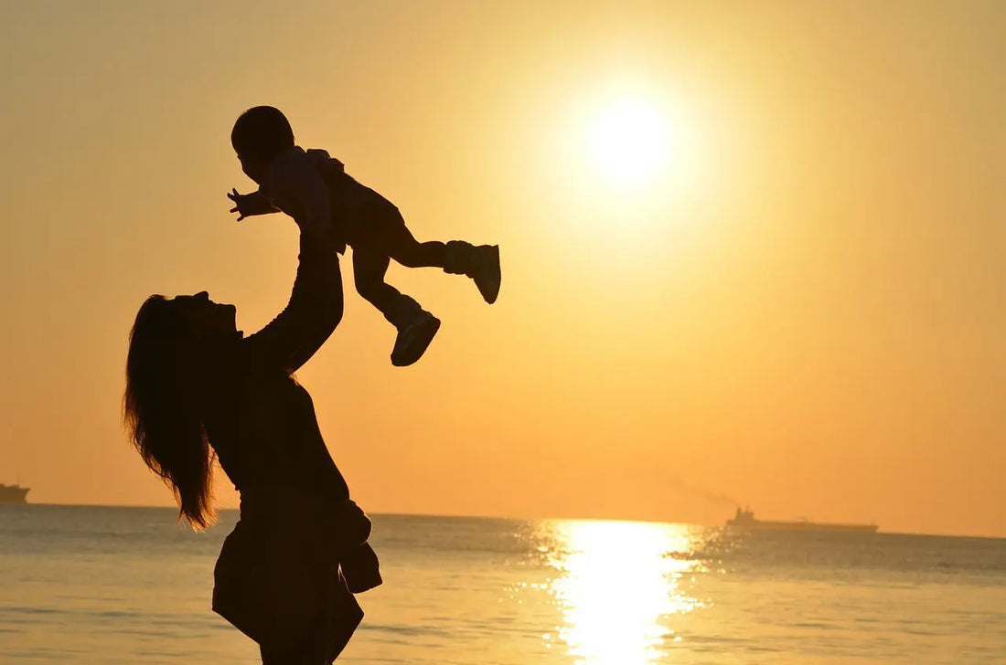 mother playing with baby infront of a lake during sunset